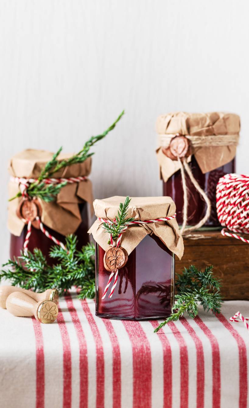 Selbstgemachte Weihnachtskonfitüre in drei hübsch verpackten Einmachgläsern auf einem festlich dekorierten Tisch