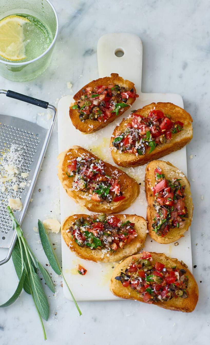 Sechs Ciabattascheiben mit Bruschettabelag nach Puttanesca-Art auf einem Holzbrett