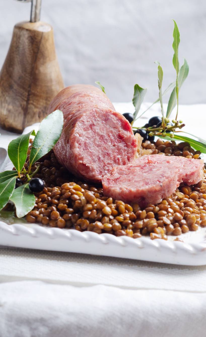 Italienische Kochwurst auf Linsengemüse angerichtet auf einem rechteckigen, weißen Teller auf einem festlich dekorierten Tisch