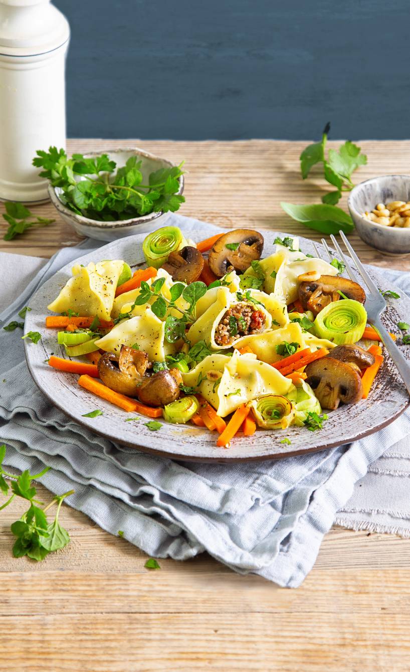 Selbstgemachte Fagottini mit Hackfleischfüllung angerichtet auf einem Teller mir Lauch-Champignon-Gemüse als Beilage