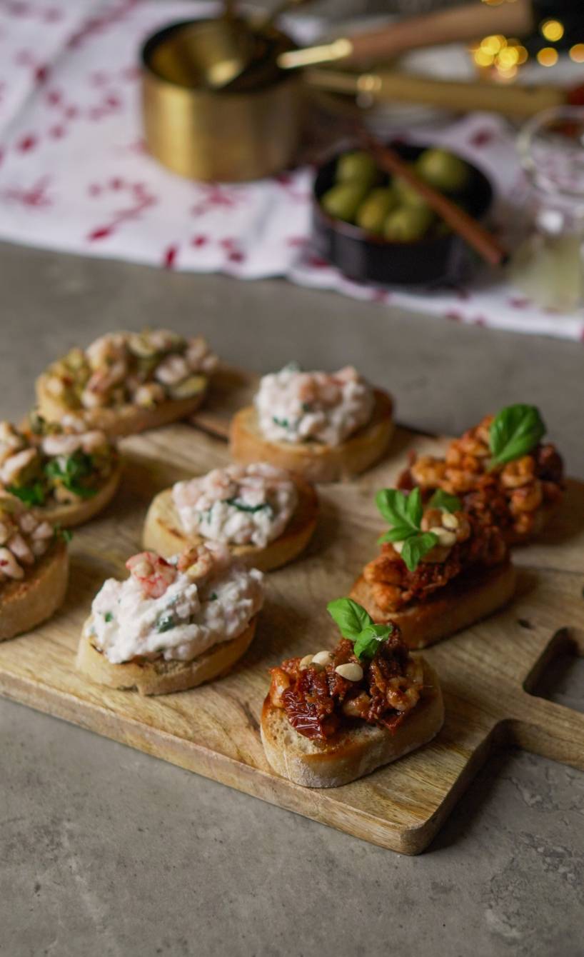 Drei verschieden belegte Krabben-Bruschette-Sorten auf einem Holzbrett arrangiert