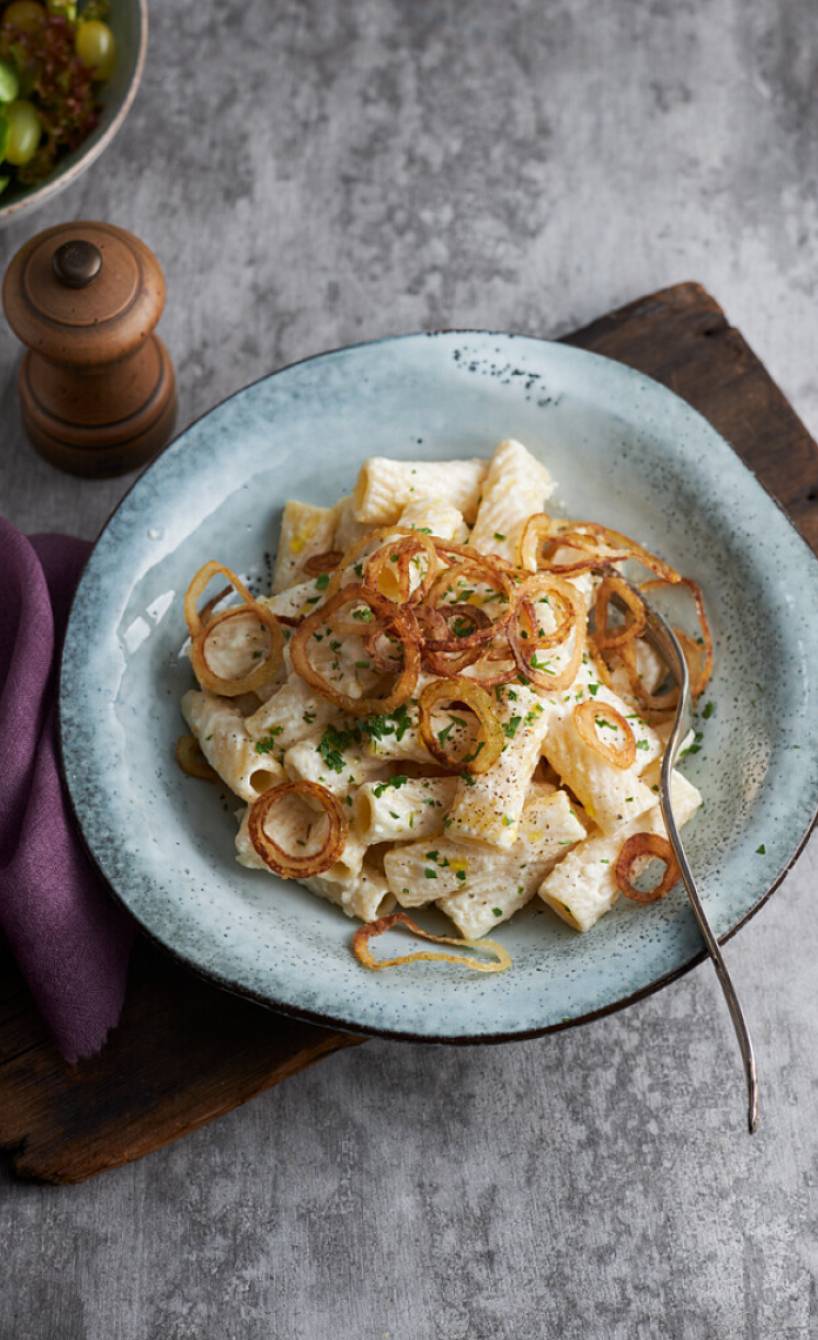 Rigatoni in cremiger weißer Soße getoppt von selbstgemachten Röstzwiebeln auf einem Teller