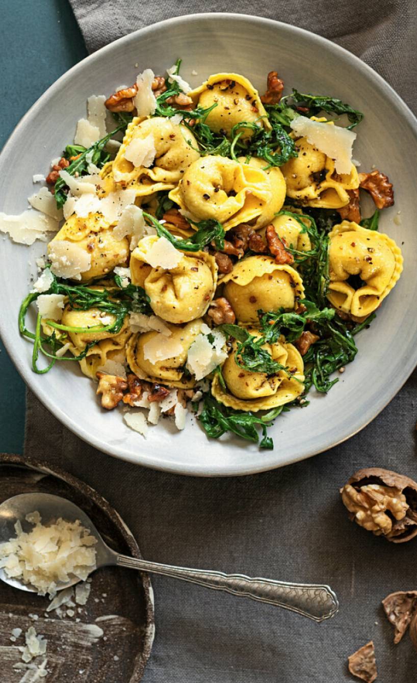 Selbstgemachte Tortellini mit Salsiccia-Füllung angerichtet auf einem Pastateller mit gebratenem Rucola und Walnüssen