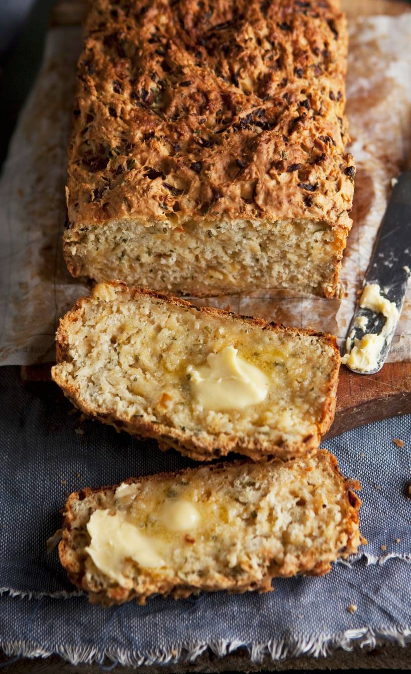 Selbstgebackenes Zwiebelbrot mit Quark und Röstzwiebeln angeschnitten auf einem Holztisch, daneben Butter
