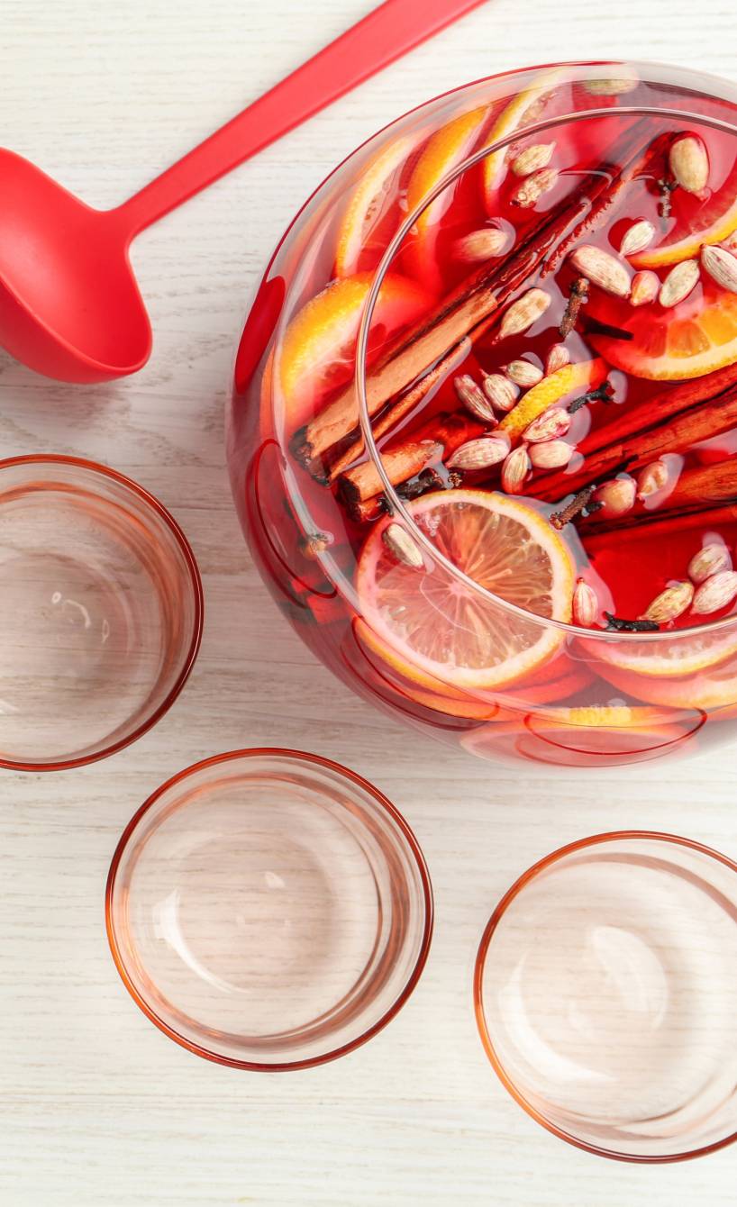 Silvesterbowle mit Früchten und Gewürzen in einer großen Glasschüssel, daneben eine Kelle und mehrere Gläser auf einem Tisch