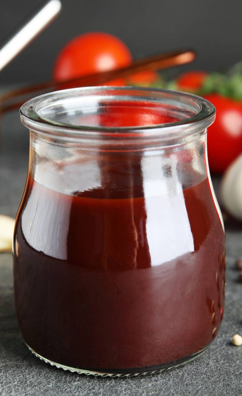 Selbstgemachte dunkle Soße in einem Einmachglas, dahinter verschiedene Zutaten und ein kupfernen Topf