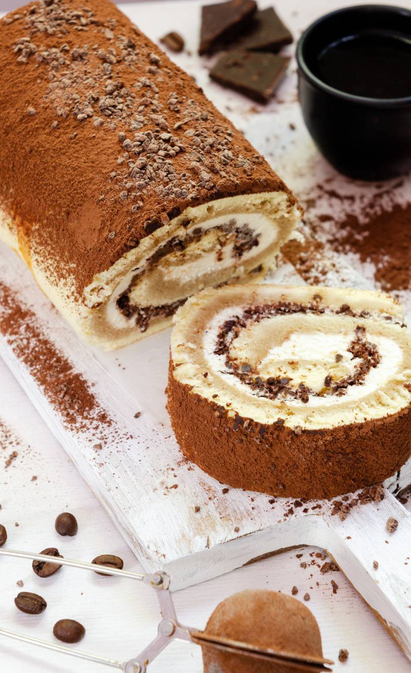 Selbst gebackene Tiramisu-Biskuitrolle angeschnitten auf einer Tortenplatte