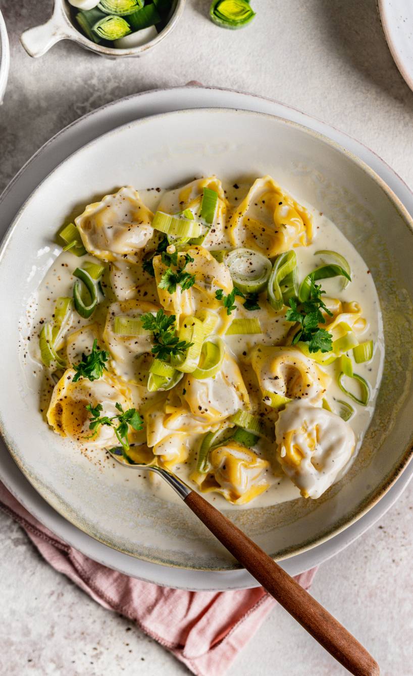 Tortellini in Käse-Lauch-Sauce angerichtet auf einem Pastateller