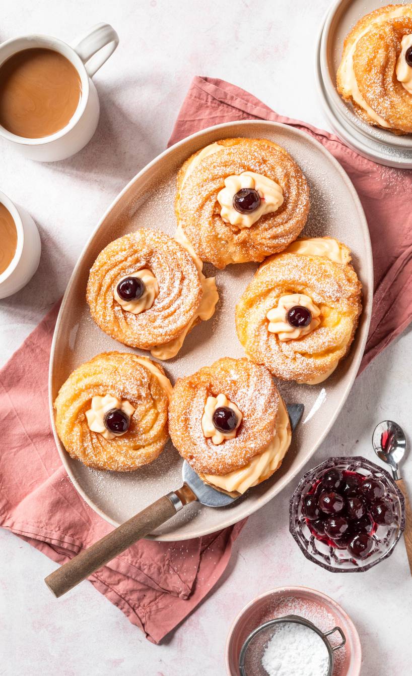 Fünf Zeppole gefüllte Brandteig-Kringel mit Vanillecreme-Füllung getoppt von Amarenakirschen auf einer Servierplatte
