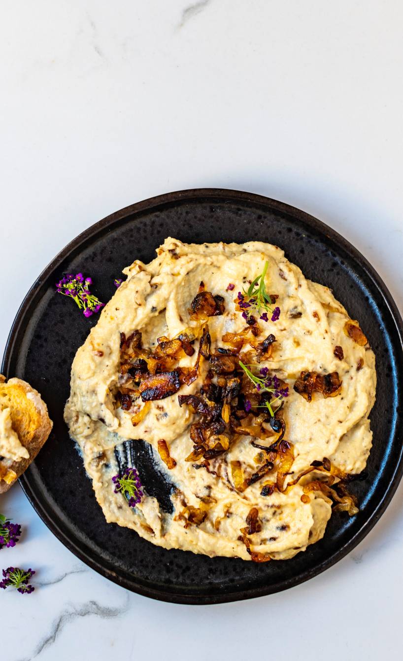Selbstgemachter Käse-Dip getoppt mit gedünsteten Zwiebeln in einer Schale, daneben geröstete Ciabattascheiben