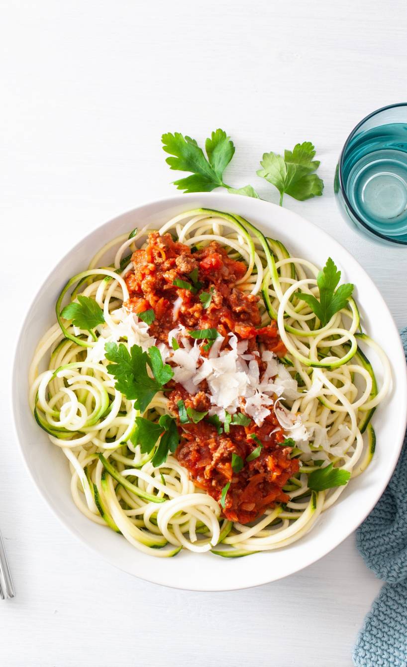 Zucchini-Nudeln mit Bolognese und Parmesan angerichtet auf einem Teller
