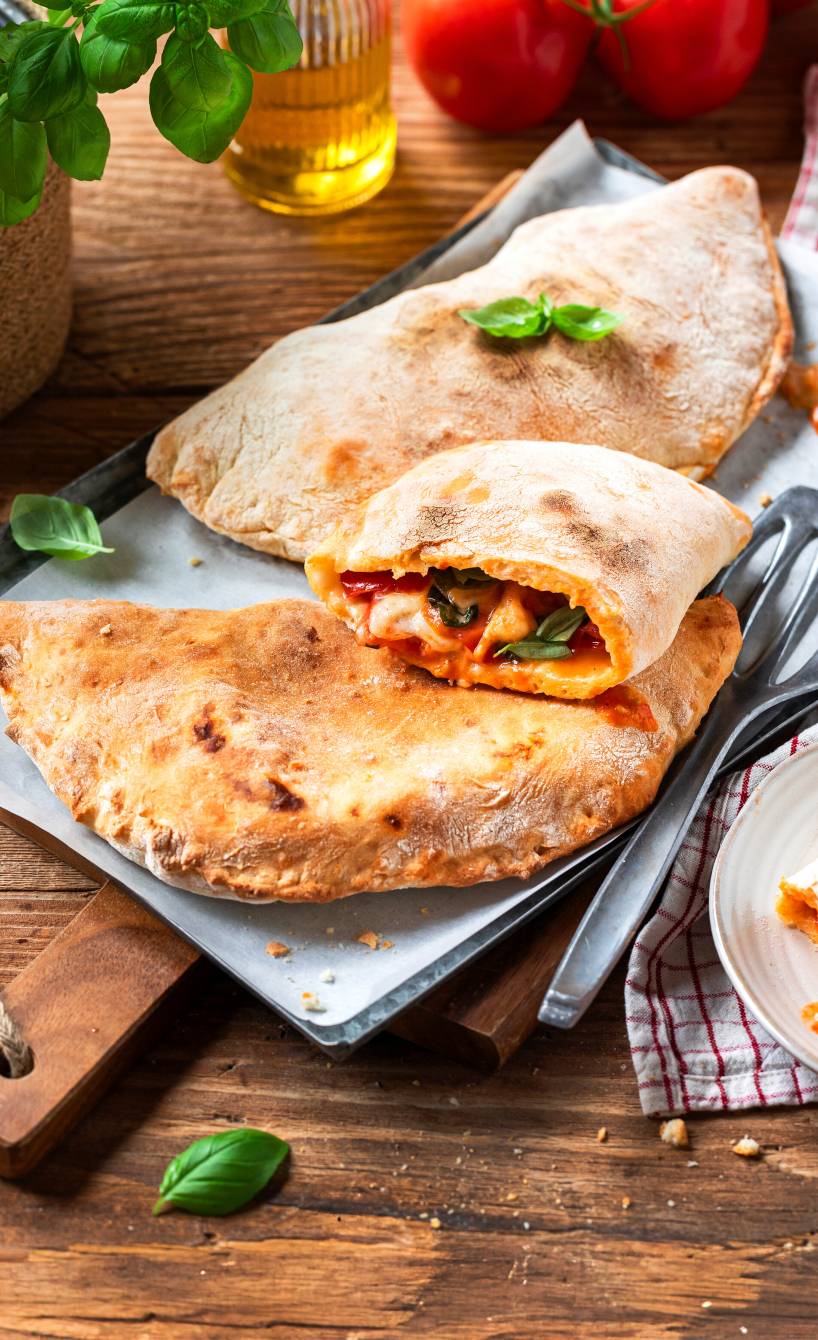 Zwei selbstgebackene Caprese-Calzonen auf einem Teller, eine halbiert mit sichtbarer Tomaten-Mozzarella-Füllung