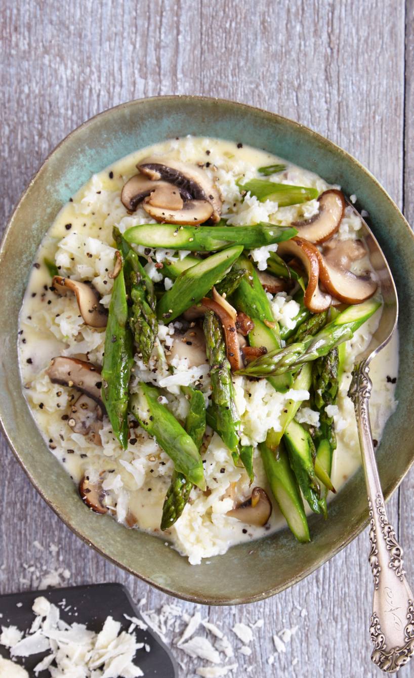 Risotto aus Blumenkohlreis mit grünem Spargel und Champignons auf einem tiefen Teller