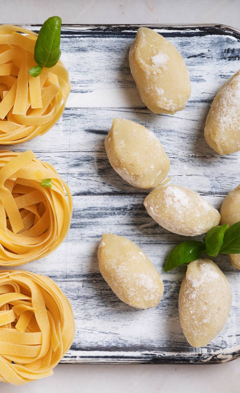 Selbstgemachte Pasta, Fusilli und Bandnudeln auf einem Tablett neben frischen Gnocchi