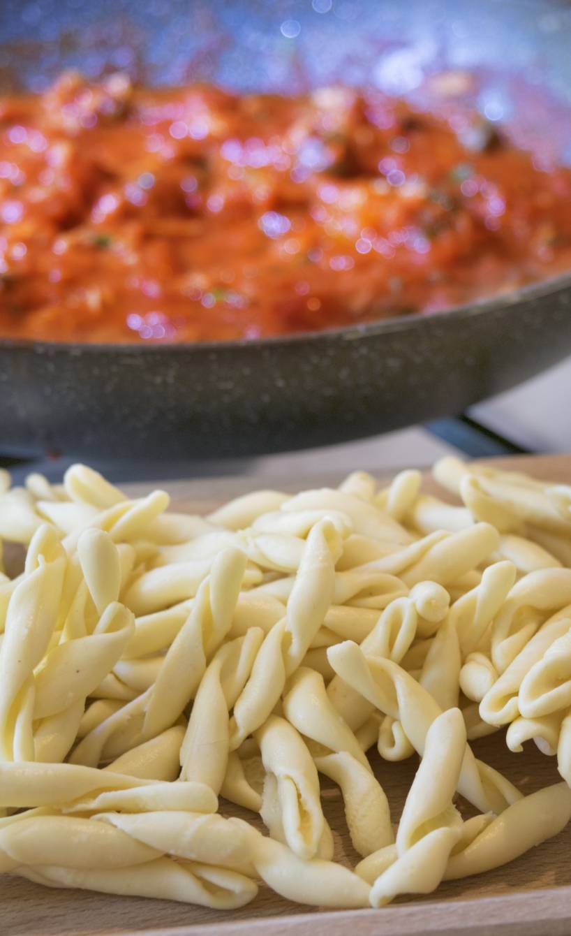 Selbstgemachte frische Nudeln auf einem Holzbrett, dahinter Tomatensoße in einer Pfanne