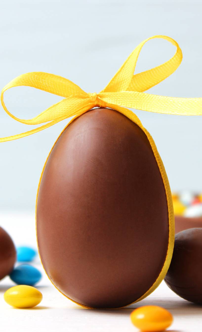 Ein großes selbstgemachtes Osterei aus Schokolade mit einem Schleifenband auf einem Tisch umgeben von mehreren kleineren Ostereiern mit Füllung
