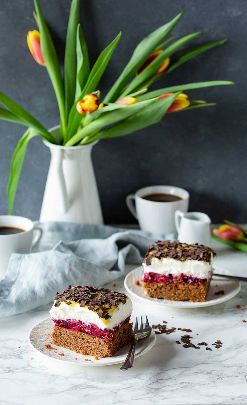 Zwei Stücke Oster-Blechkuchen mit Sahne, Kirschkompott und Eierlikör-Topping auf Kuchentellern
