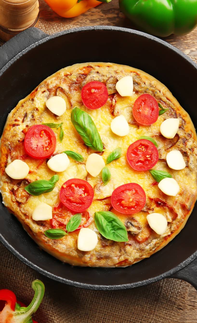 Gebackene Pfannenpizza auf einem Holztisch umgeben von frischen Zutaten