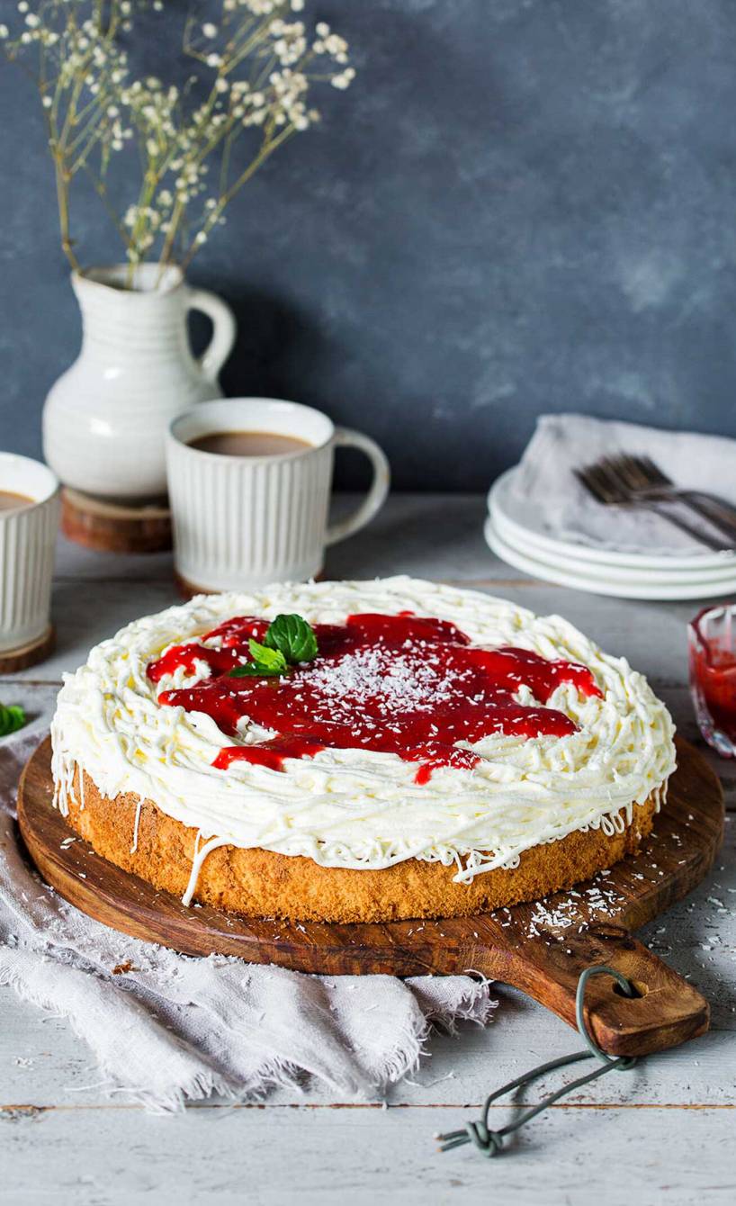 Runder Spaghettikuchen getoppt mit Erdbeersoße und Kokosraspeln auf einer Kuchenplatte