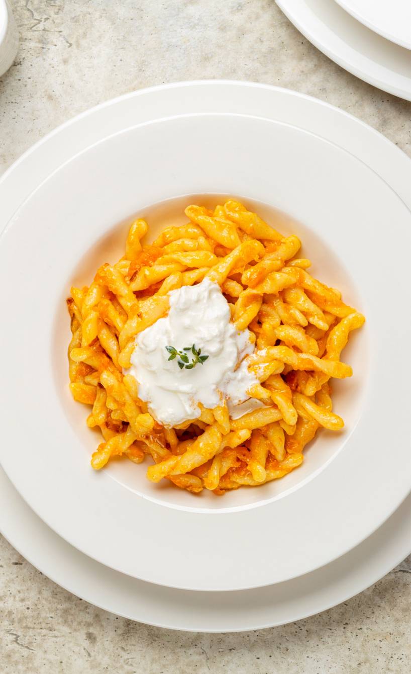 Strozzapreti mit Kürbissoße auf einem Pastateller getoppt von Stracciatella-Käse