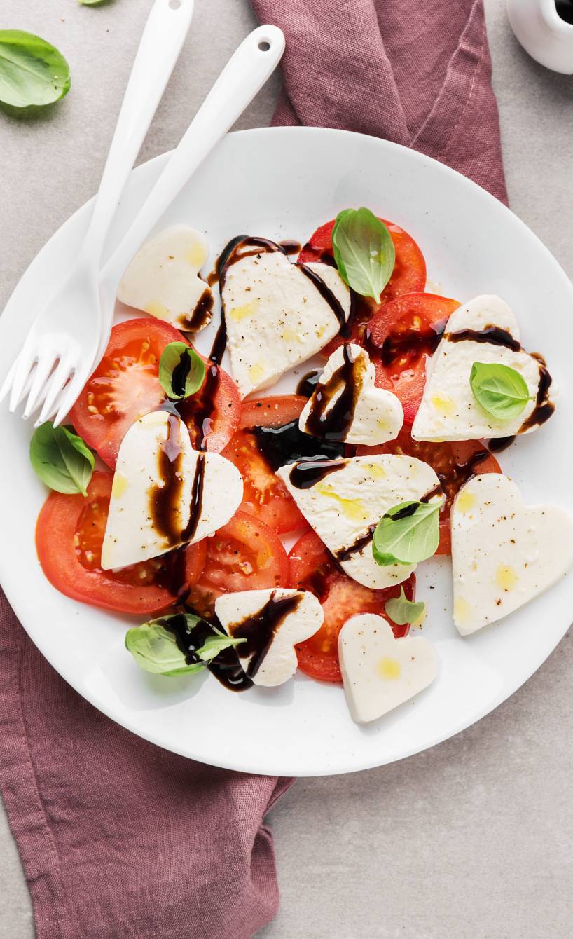 Caprese-Salat aus Tomaten und Mozzarellaherzen angerichtet auf einem Teller für den Valentinstag