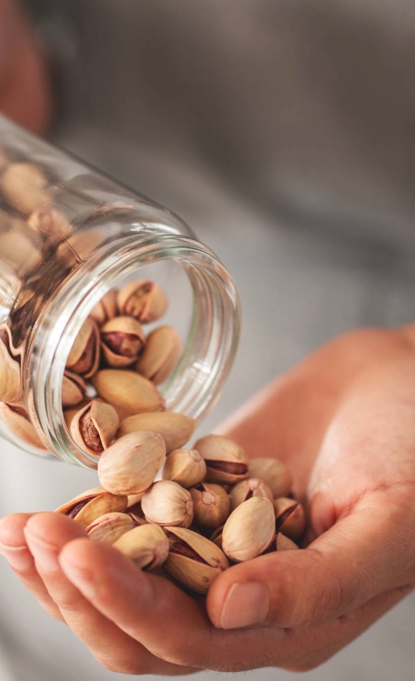 Jemand entnimmt eine Hand voll Pistazien aus einem Einmachglas Jemand entnimmt eine Hand voll Pistazien aus einem Einmachglas