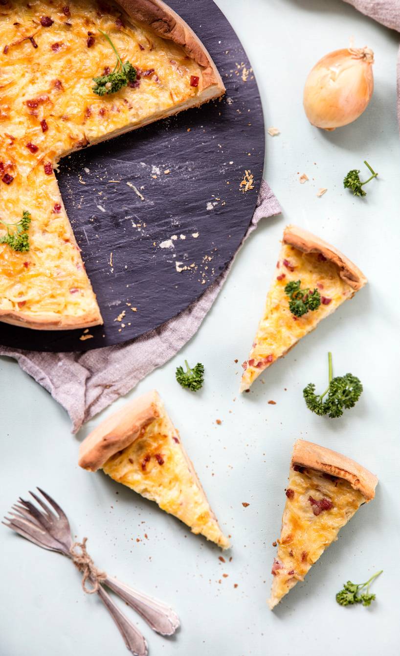 Selbstgebackener runder Zwiebelkuchen angeschnitten auf einer Schieferplatte