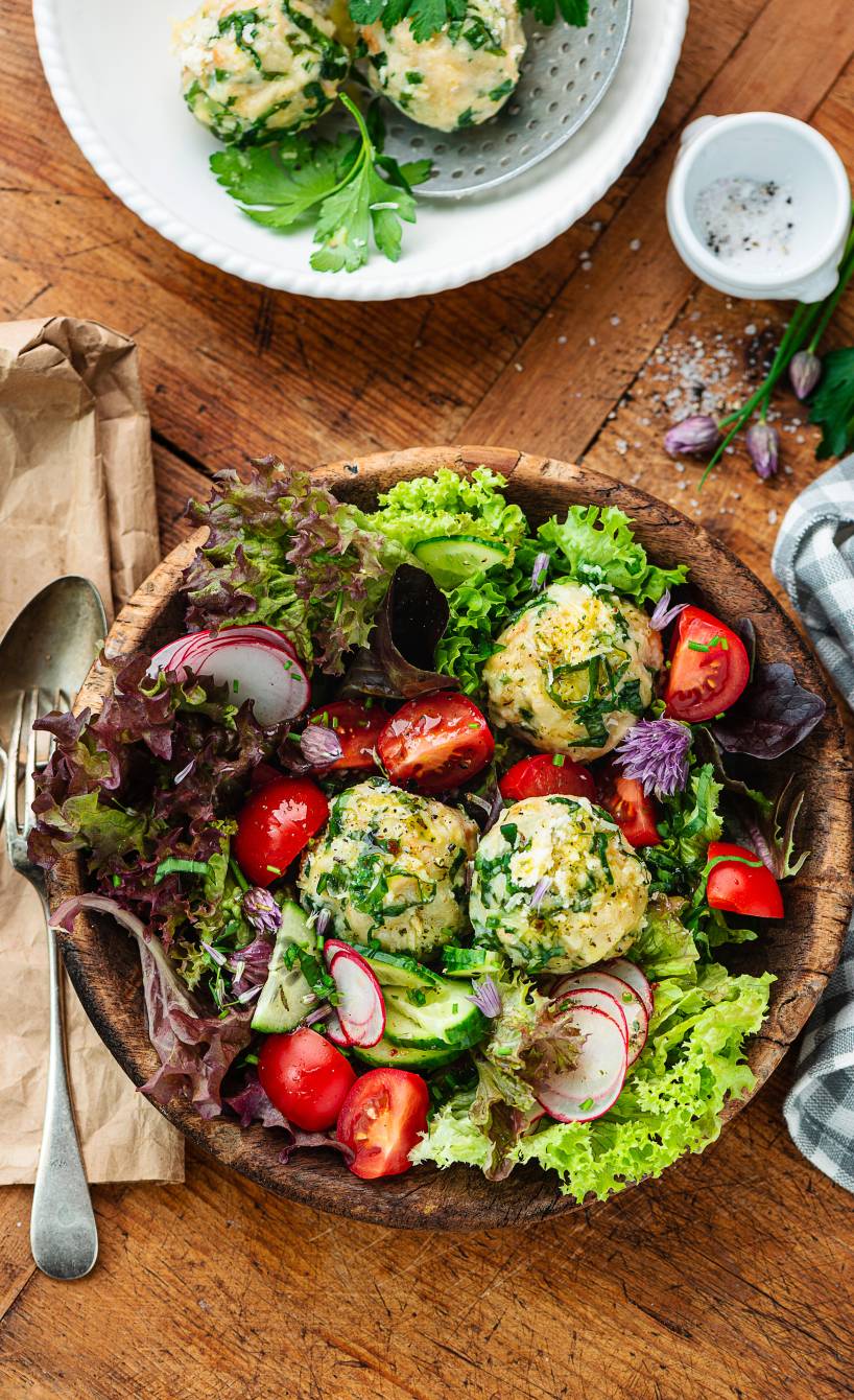 Mehrere selbstgemachte Bärlauchknödel angerichtet auf einem buntem Frühlingssalat