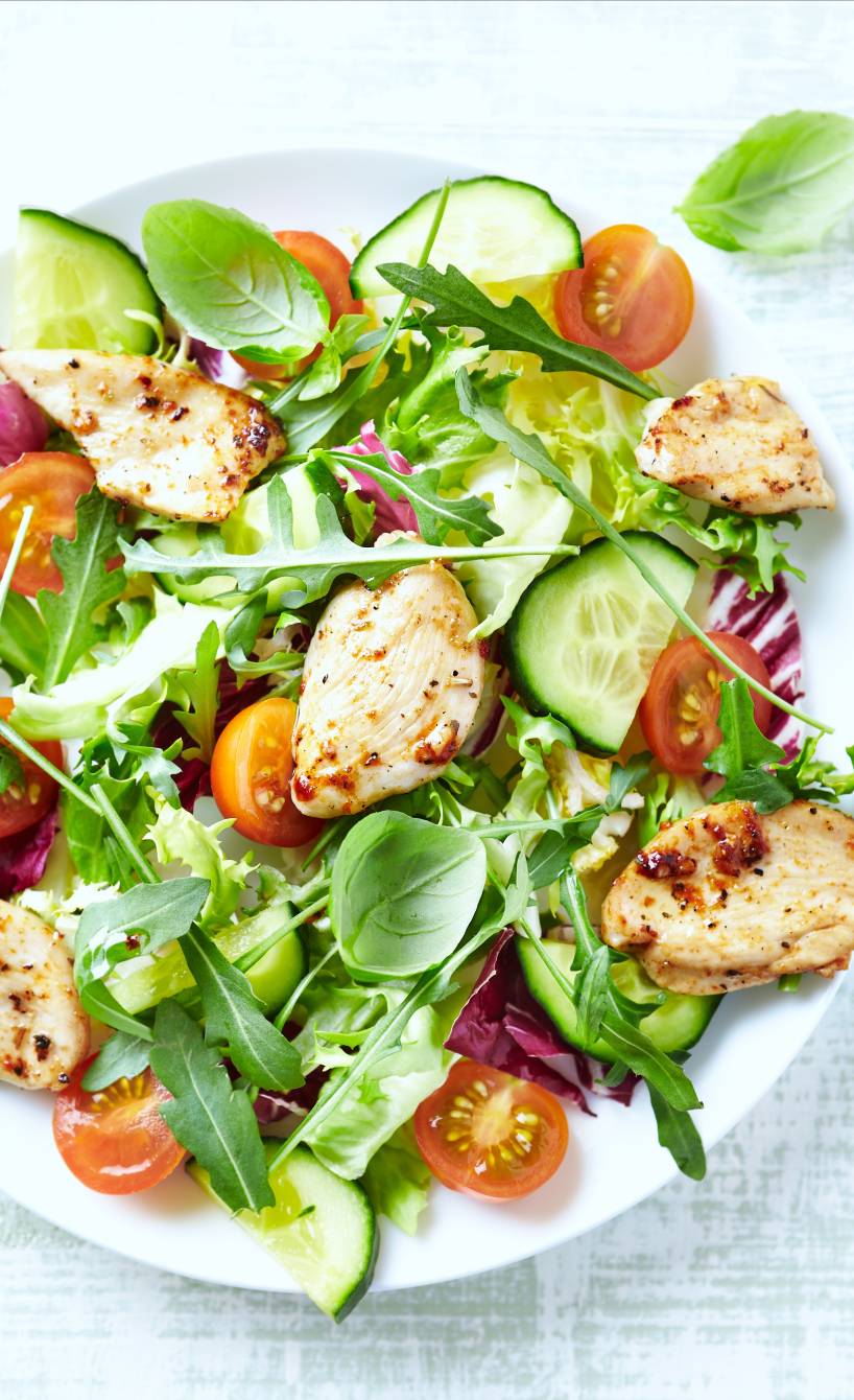 Gemischter bunter Salat getoppt von gebratenen, marinierten Putenbruststücken auf einem Teller