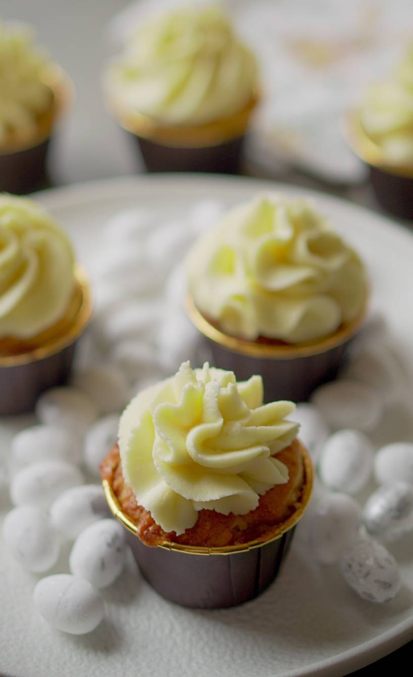 Mehrere Muffins mit Eielikörtopping auf einer Servierplatte auf einem Tisch mit Osterdeko