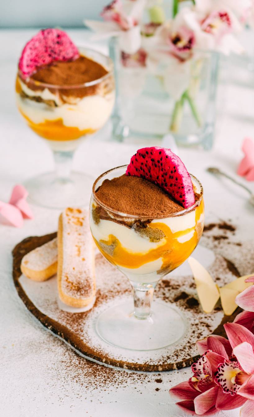 Zwei Gläser mit  Eierlikör-Tiramisu mit Mascarpone und Quark dekoriert mit Drachenfrucht-Scheiben auf einem Tisch