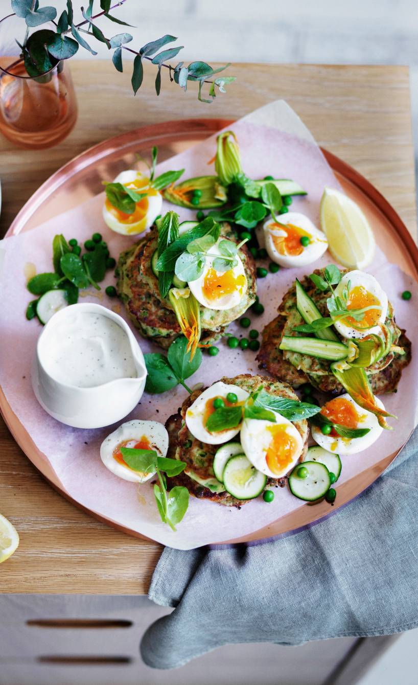Mehrere Zucchini-Puffer mit Joghurt und Feta getoppt von wachsweichen, halbierten Eiern angerichtet auf einem Teller