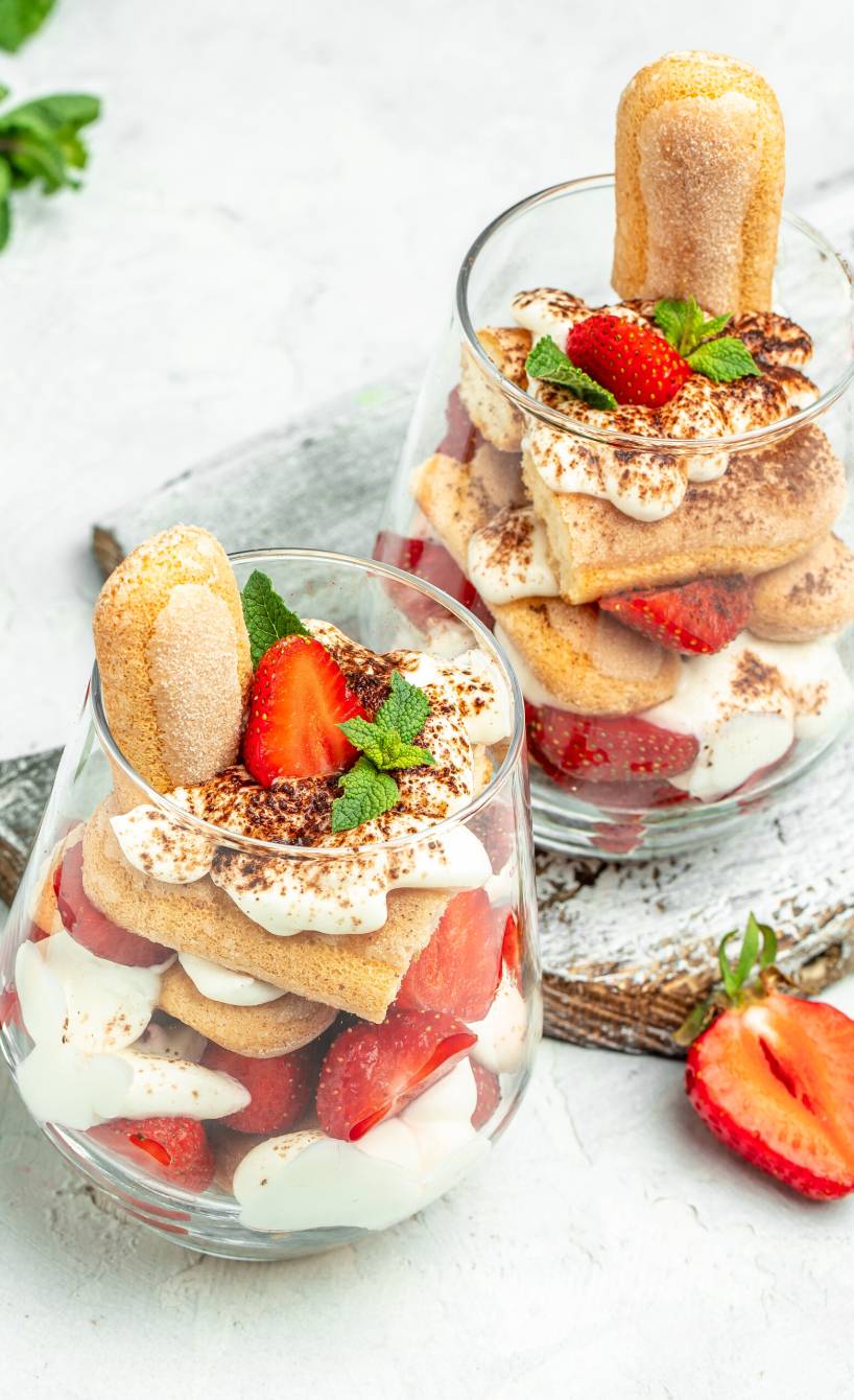 Zwei Gläser mit Erdbeer-Tiramisu mit Mascarpone und Quark garniert mit frischen Minzblättern auf einem Tisch