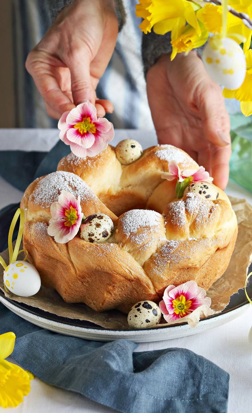 Selbstgebackener Hefekranz auf einem Tisch wird gerade mit Osterdeko verschönert