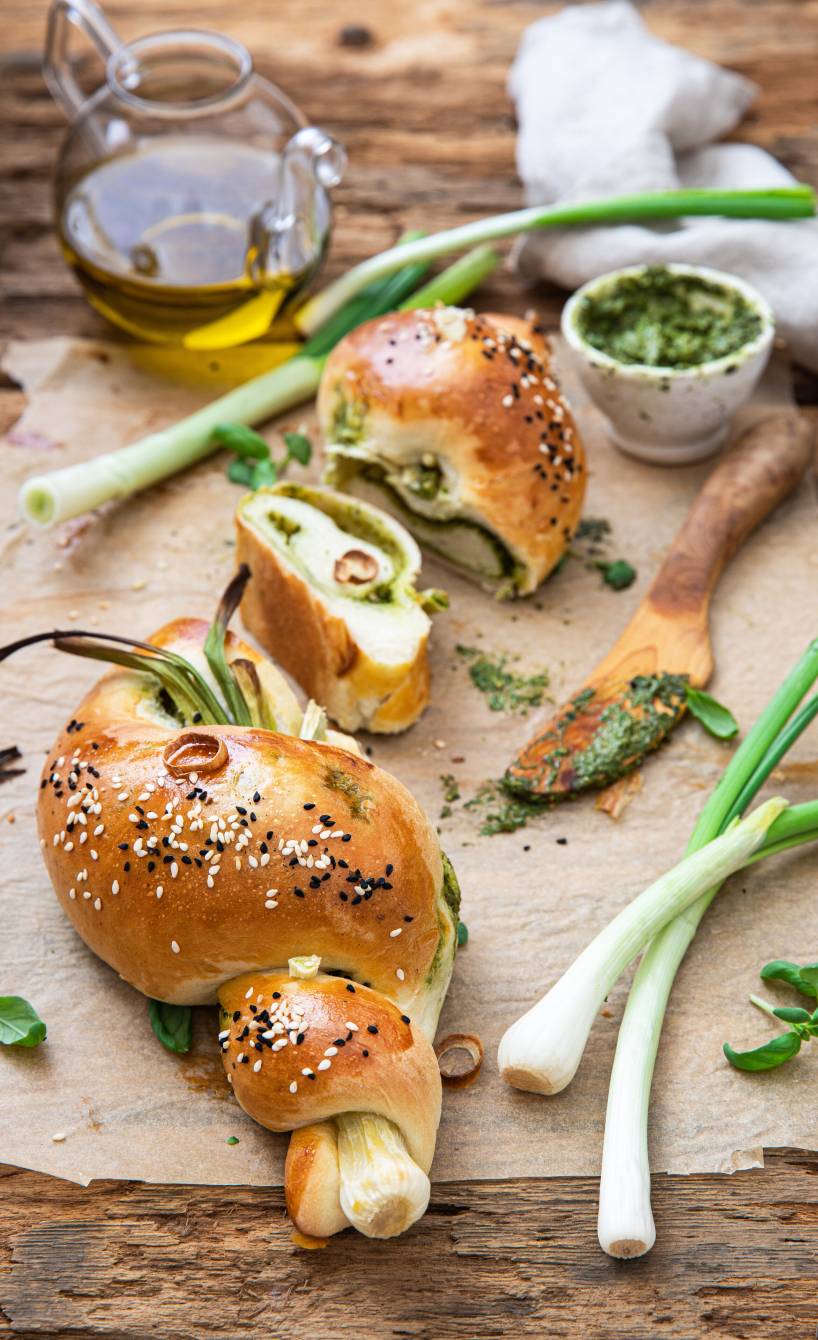 Ein gefülltes Frühlingszwiebelbrötchen mit Basilikumpesto angeschnitten auf einem Holzbrett