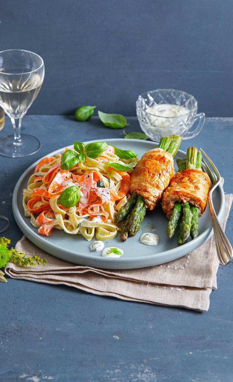 Zwei Hähnchen-Involtini mit grünem Spargel angerichtet auf einem Teller neben Karotten-Tagliatelle in cremiger Sauce