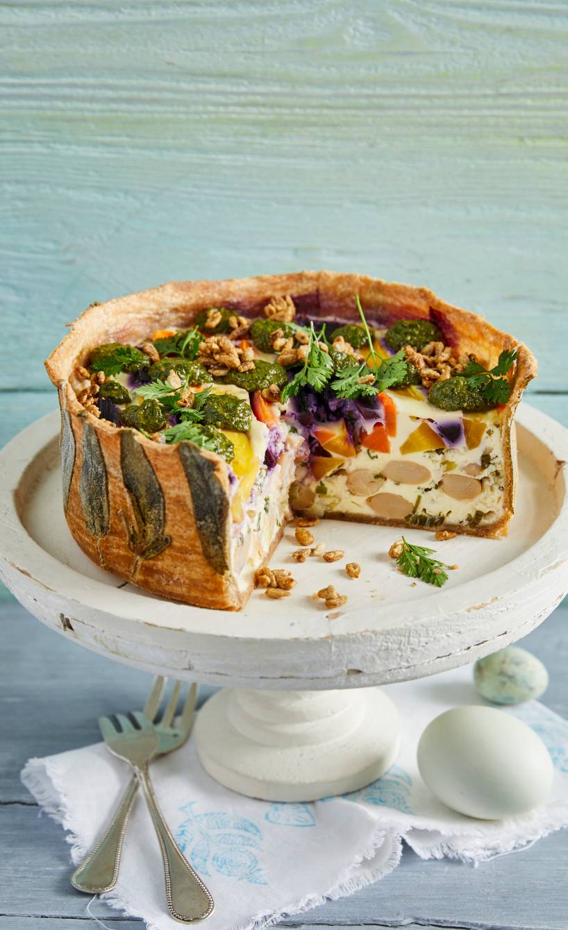 Selbstgebackene Möhren-Quiche mit Bohnen getoppt von Basilikumpesto und karamellisierten Sonnenblumenkernen angeschnitten auf einer Tortenplatte
