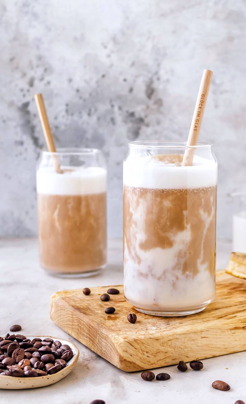 Zwei Gläser mit selbstgemachtem Bananen-Eiskaffee auf einem Holzbrett