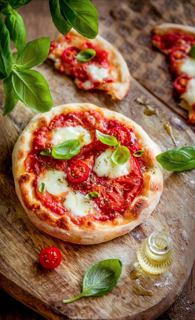 Zwei italienische Pizzette Margherita Mini-Pizzen garniert mit frischem Basilikum auf einem Holzbrett 