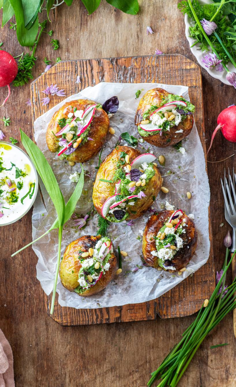 Fünf gebackene Ofenkartoffeln gefüllt mit Bärlauch-Frischkäse getoppt von Feta und Pinienkernen auf einem Holzbrett
