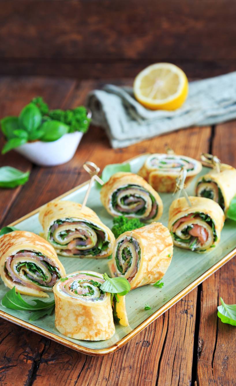 Schnelle Crespelle-Häppchen mit Rucola, Frischkäse und Räucherlachs angerichtet auf einer Servierplatte