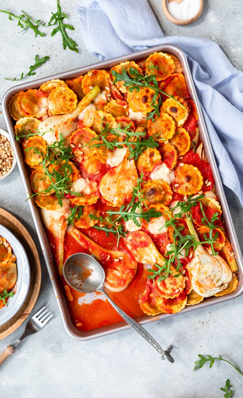 Ravioli mit Fenchel, Rucola und Mozzarella in pikanter Tomatensoße auf einem Backblech