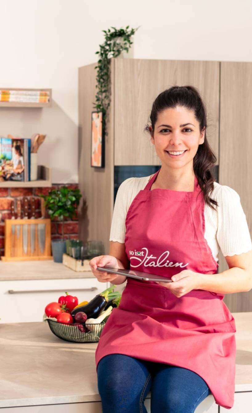 Serena Loddo sitzt auf der Kücheninsel in der So isst Italien Küche und sucht auf dem Tablet nach Rezepten für Ostern