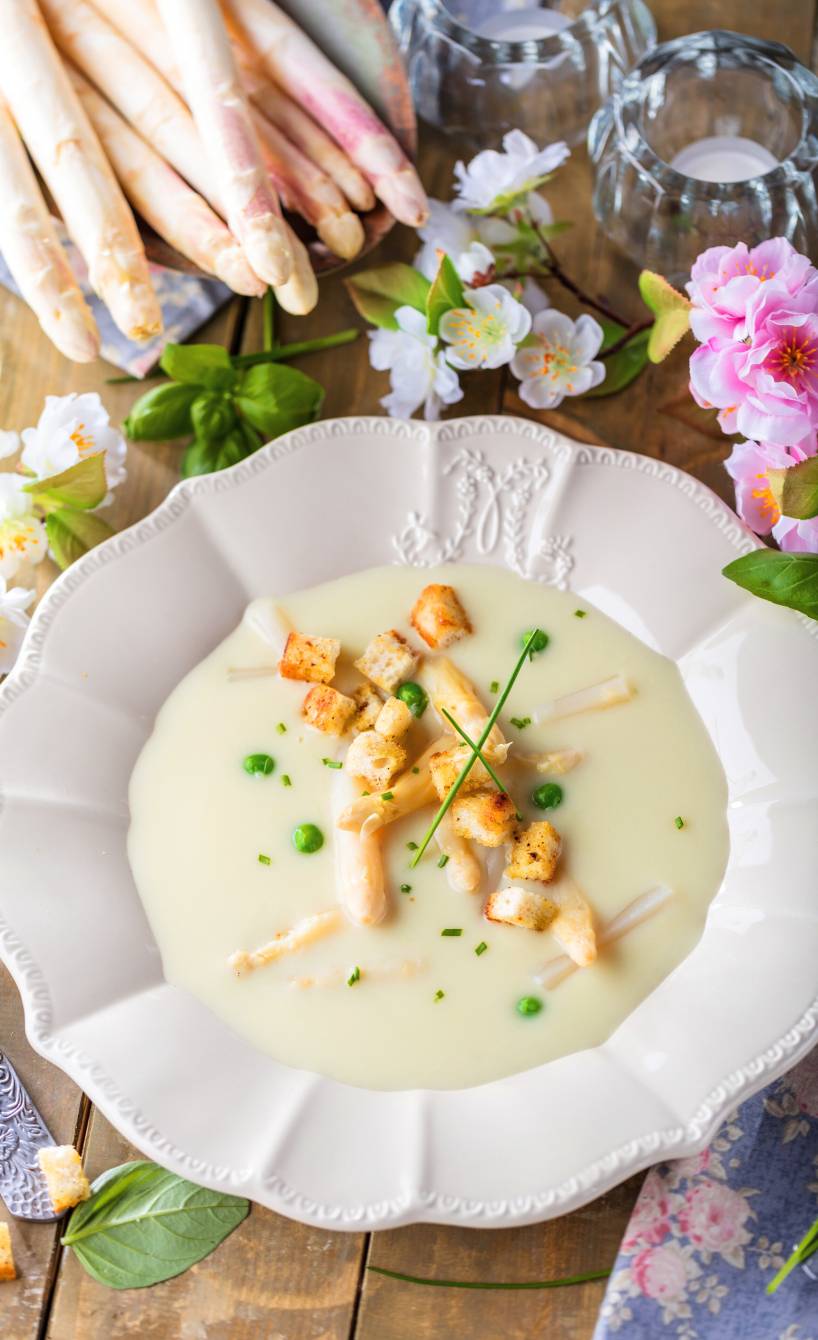 Spargelcremesuppe angerichtet auf einem tiefen Teller getoppt von Erbsen, Spargelspitzen und Croûtons Spargelcremesuppe angerichtet auf einem tiefen Teller getoppt von Erbsen, Spargelspitzen und Croûtons