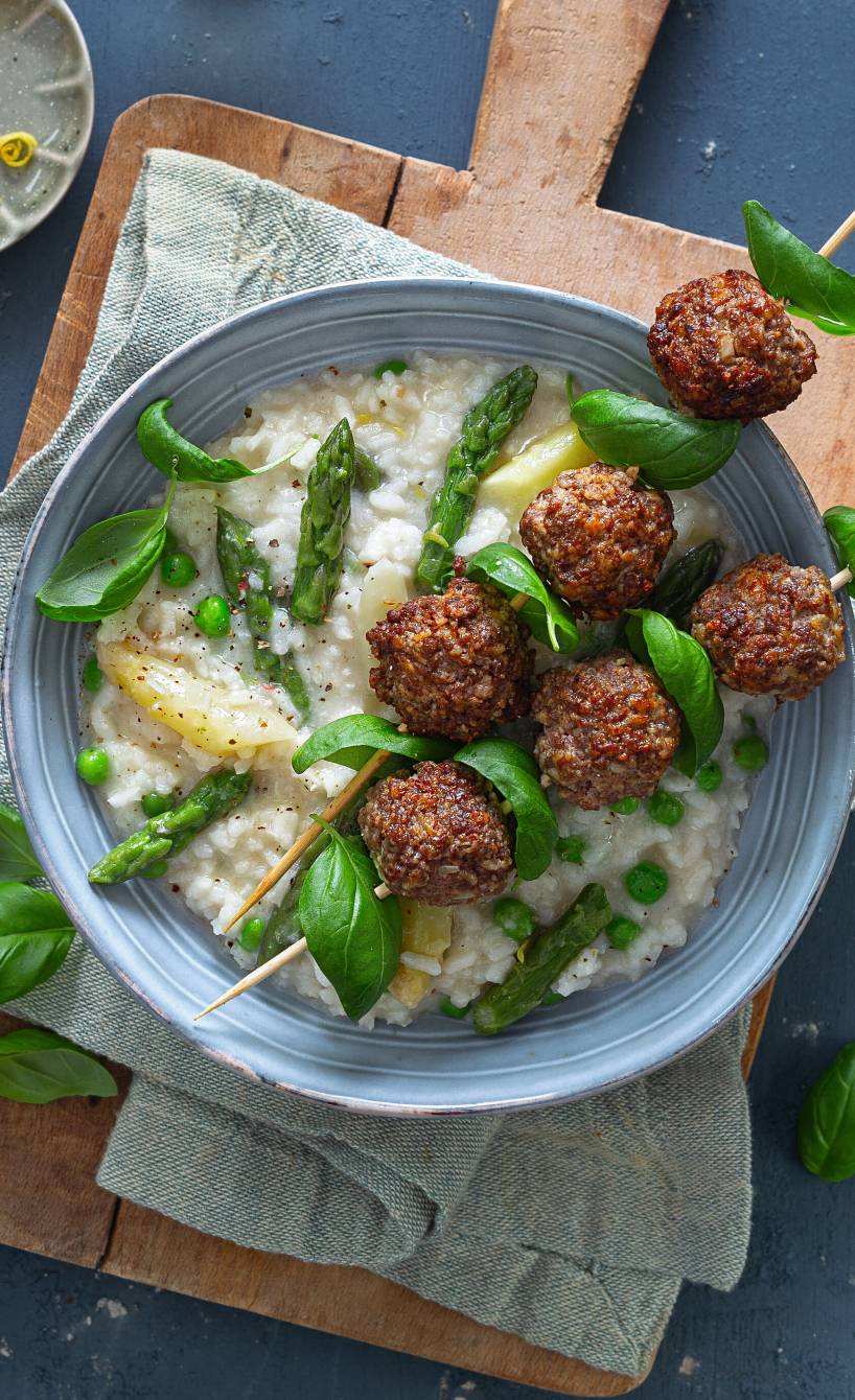 Risotto mit weißem und grünem Spargel in einer Schale, auf der zwei Hackbällchen-Spießen liegen