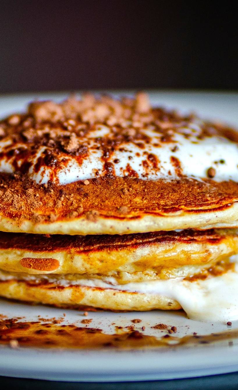 Tiramisu-Pancakes geschichtet mit Mascarponecreme und bestäubt mit Kakaopulver auf einem Teller