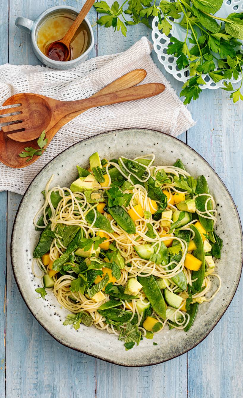 Veganer Nudelsalat aus Capellini mit Avocado, Mango und Gurke angerichtet auf einem großen Teller