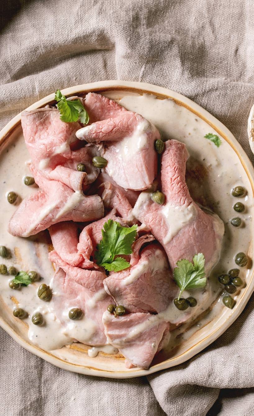 Selbstgemachtes Vitello tonnato angerichtet auf einem Vorspeisenteller, daneben Thunfischsauce und Kapern