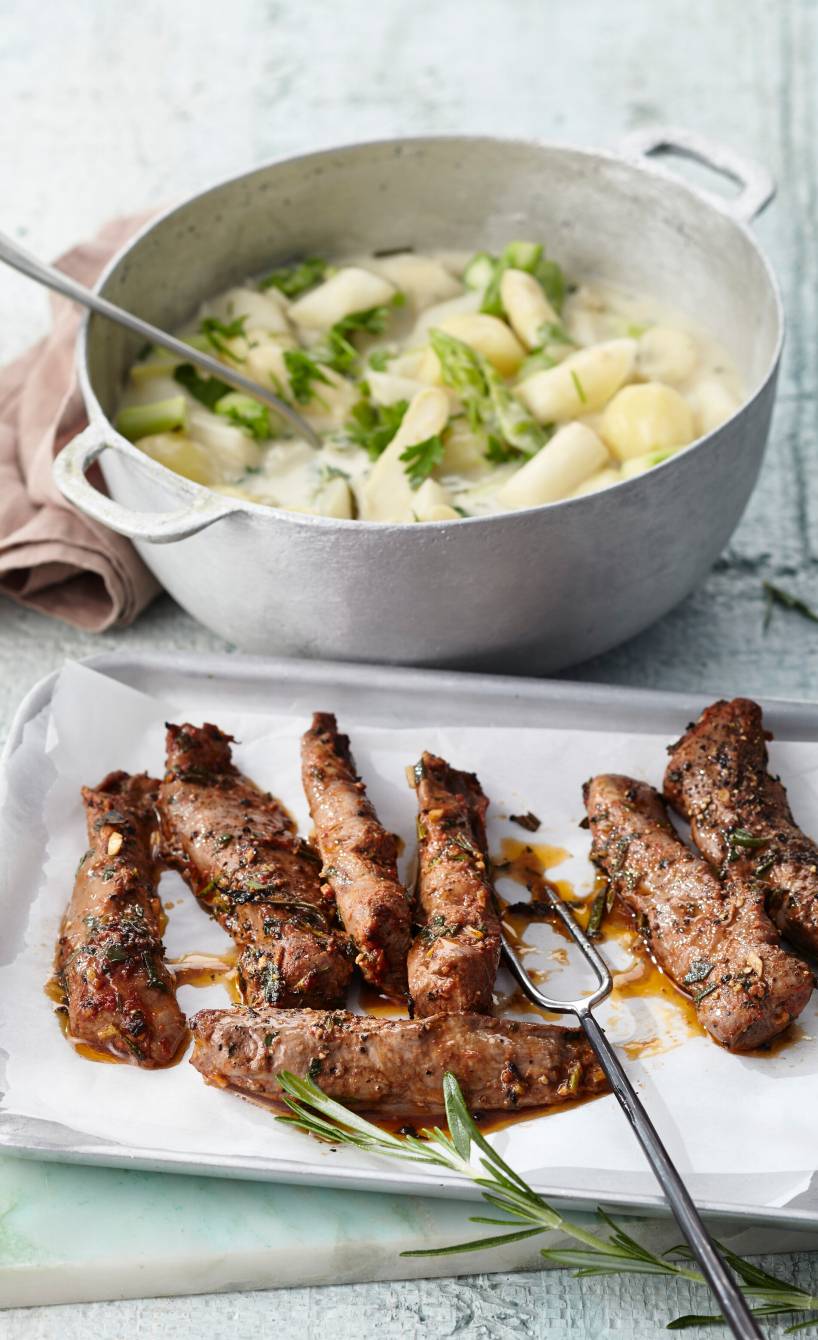 Mehrere im Ofen gegrillte Lammfilets auf einer Servierplatte, daneben Kartoffel-Spargelragout auf einem Tisch