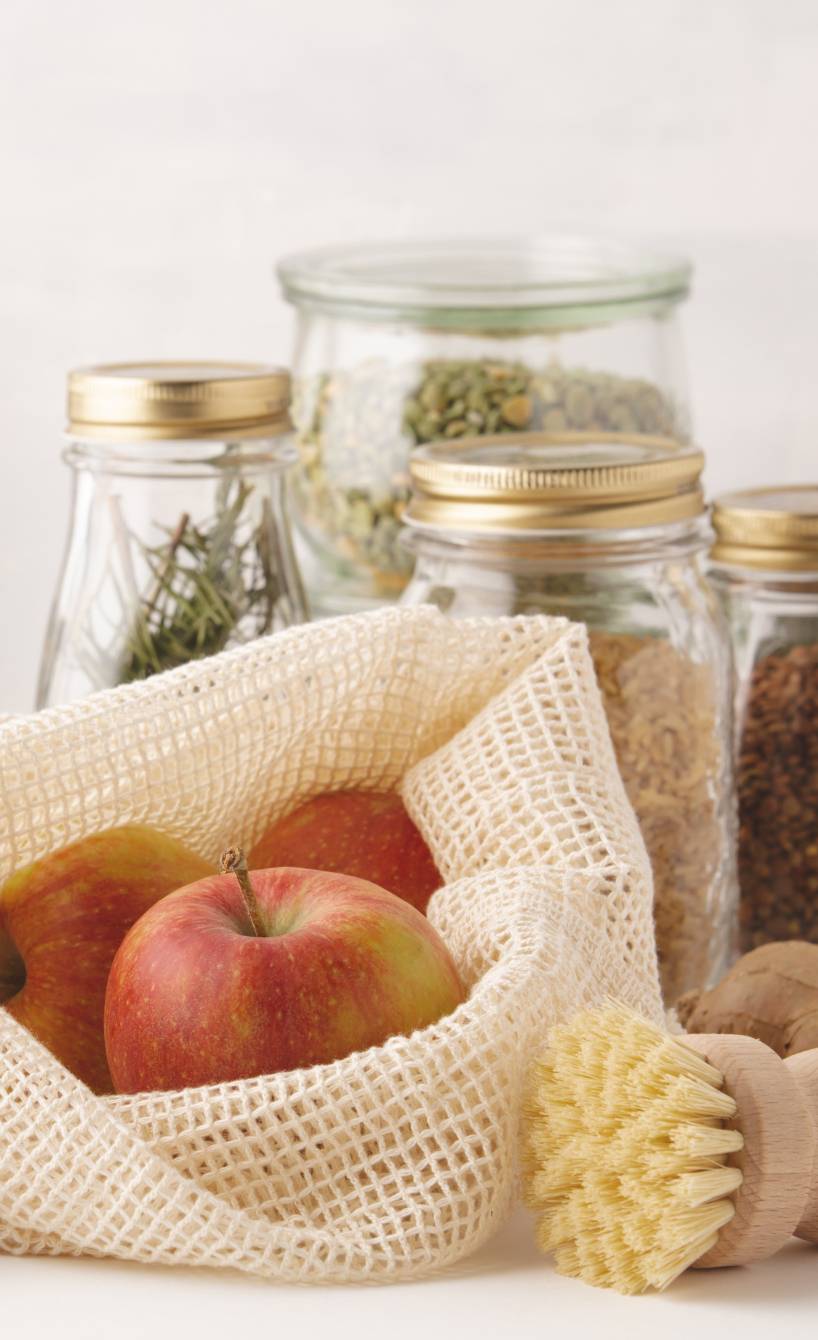 Obst und Gemüse in Stoffnetzen und Gläsern auf einem Tisch vor einer Tafel, auf der Zero Waste steht